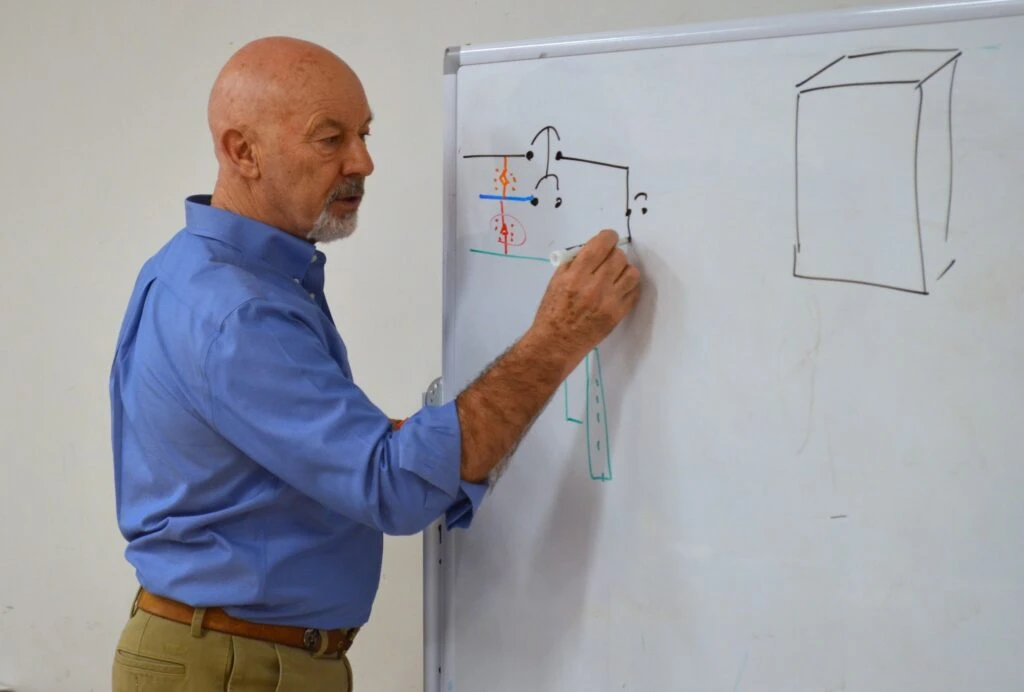Instructor Roger Hellyar-Brook draws an electrical diagram at a white board.