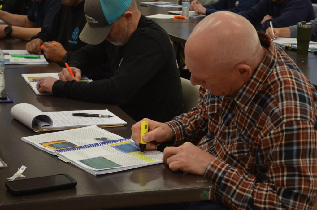 A person sits at a table and highlights text in their ABYC Electrical study guide.