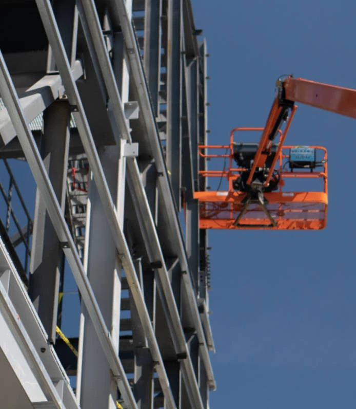 orange construction lift in air next to steel build construction