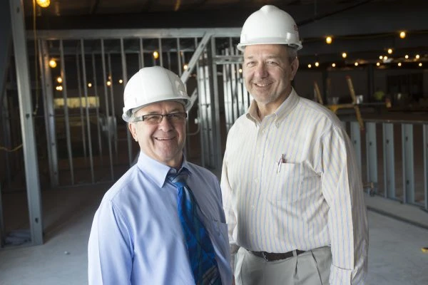 Two men in construction hats smiling inside of a building during construction