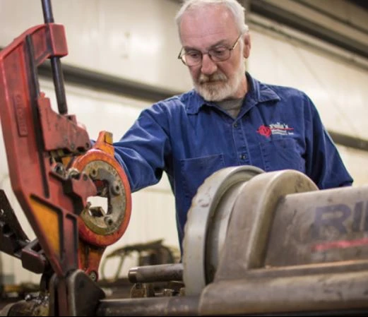 Experienced Peña Mechanical technician using a pipe threading machine to cut threads into industrial piping