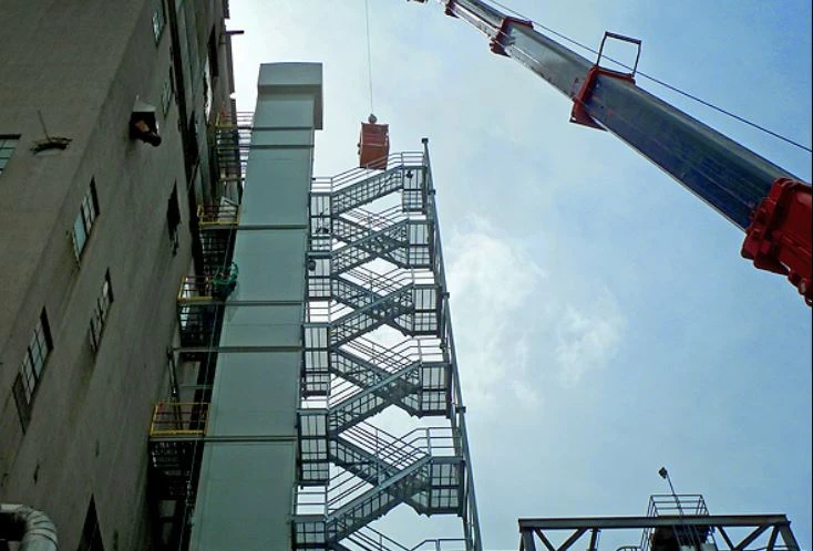 Pena's Mechanical millwrights installing metal staircase using hydraulic crane and man basket on industrial site