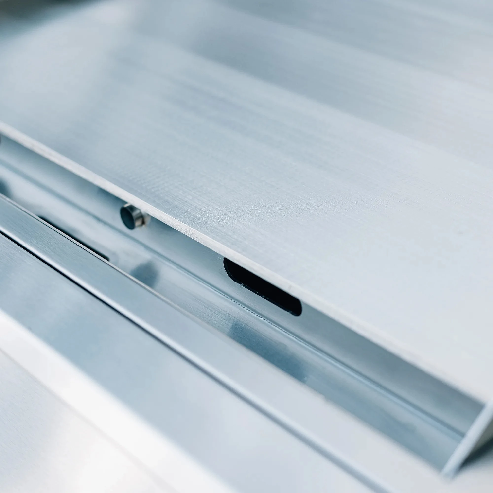 Close-up of the full-width stainless steel drip tray and grease drain slot on the Summerset 30-inch Griddle Pro built-in gas griddle