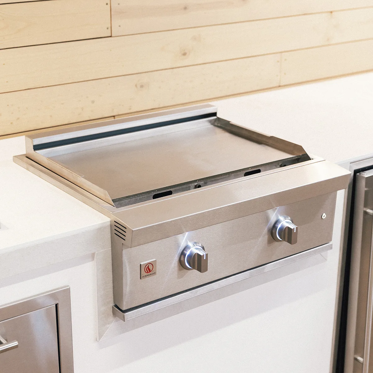 Summerset GRID30 30-inch built-in gas griddle installed in a white outdoor kitchen counter against a light wood shiplap wall