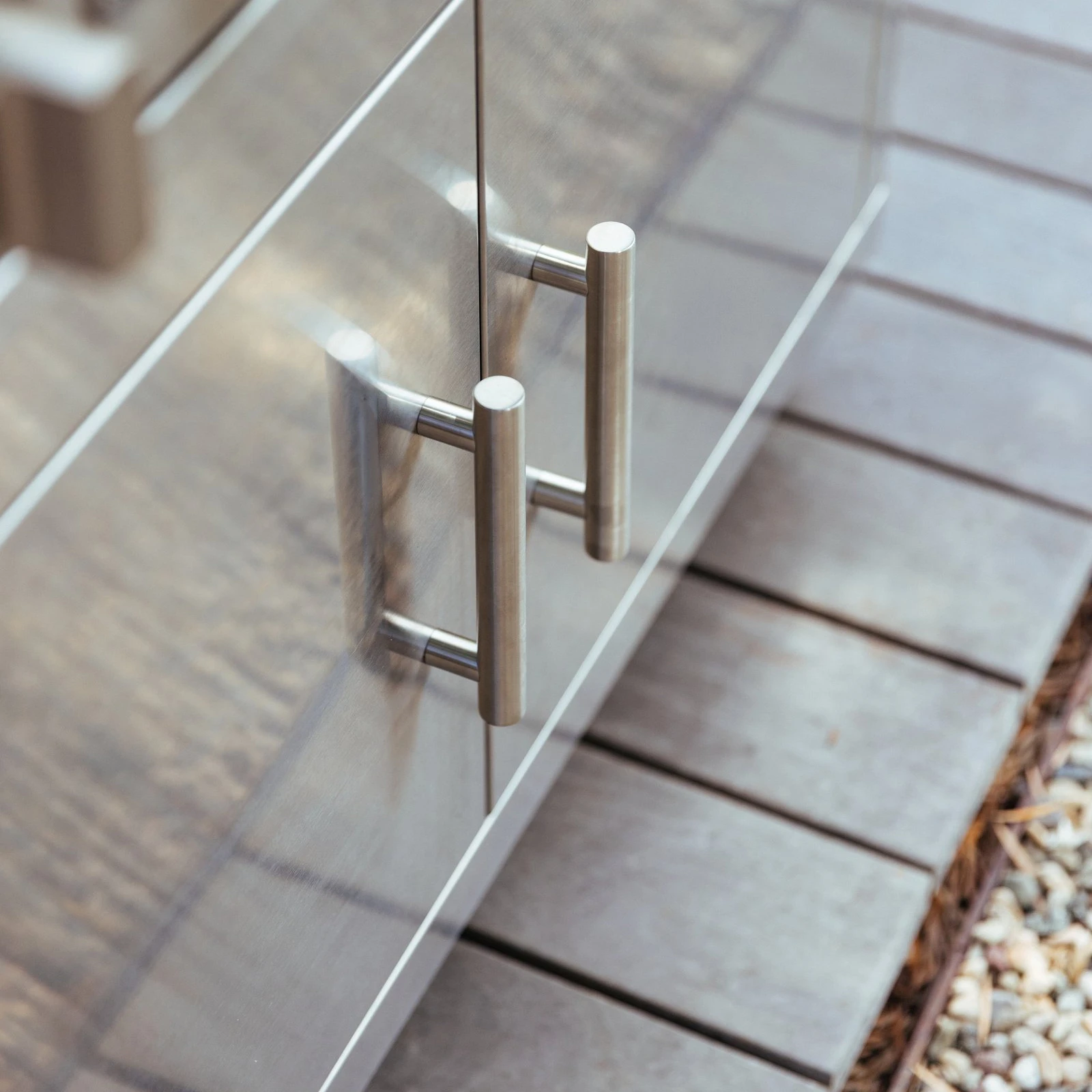 Close-up of the stainless steel double door pull handles on a Summerset grill cart, mounted on an outdoor patio