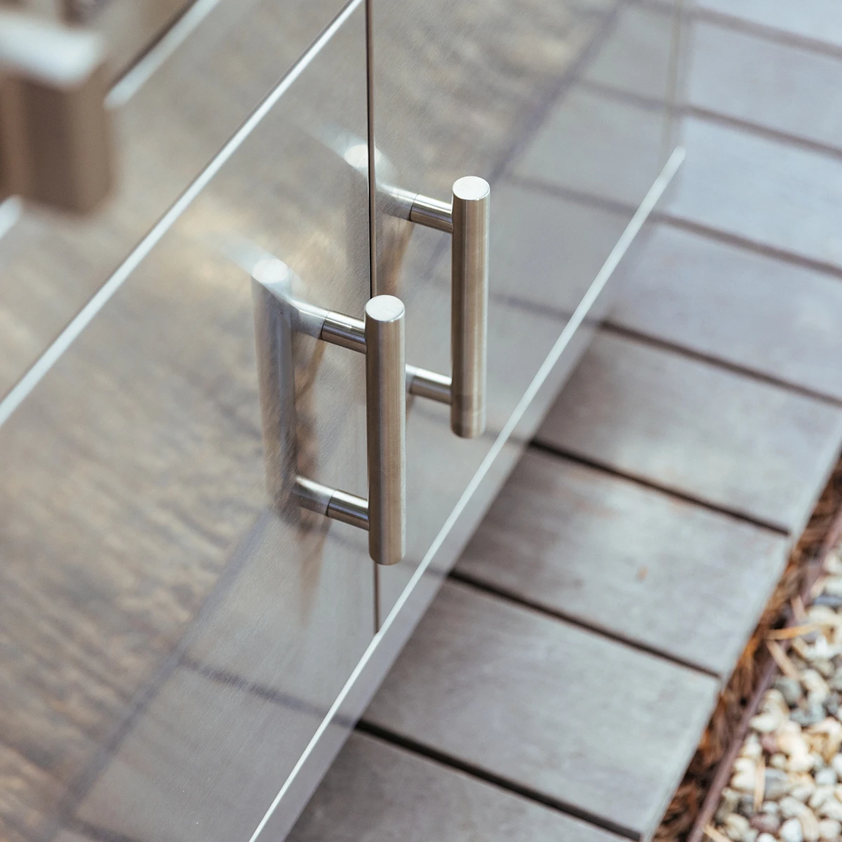 Close-up of the stainless steel double door pull handles on a Summerset grill cart, mounted on an outdoor patio