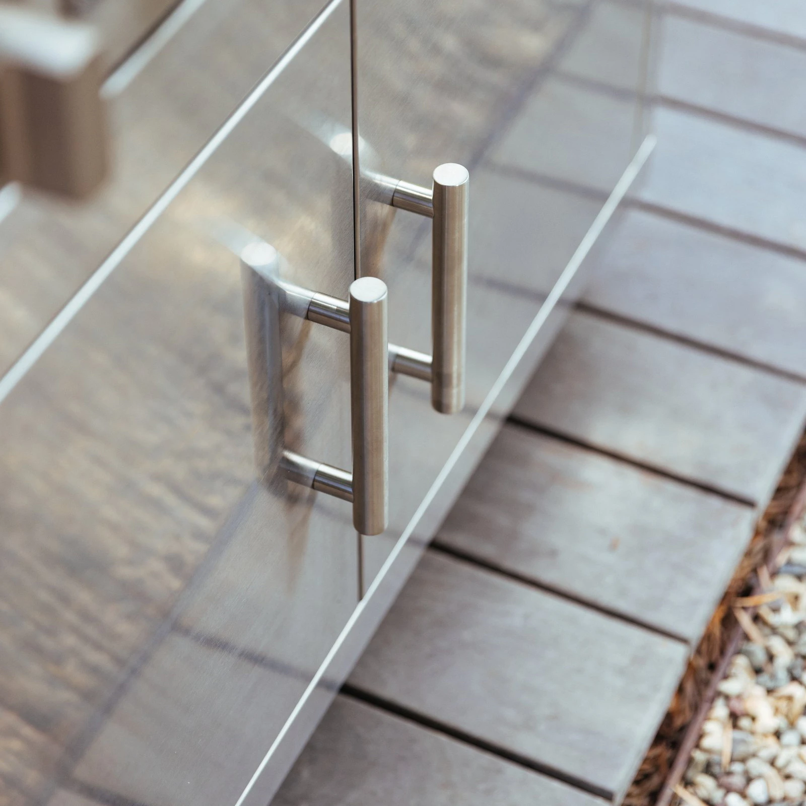 Close-up of the stainless steel double door pull handles on a Summerset grill cart, mounted on an outdoor patio