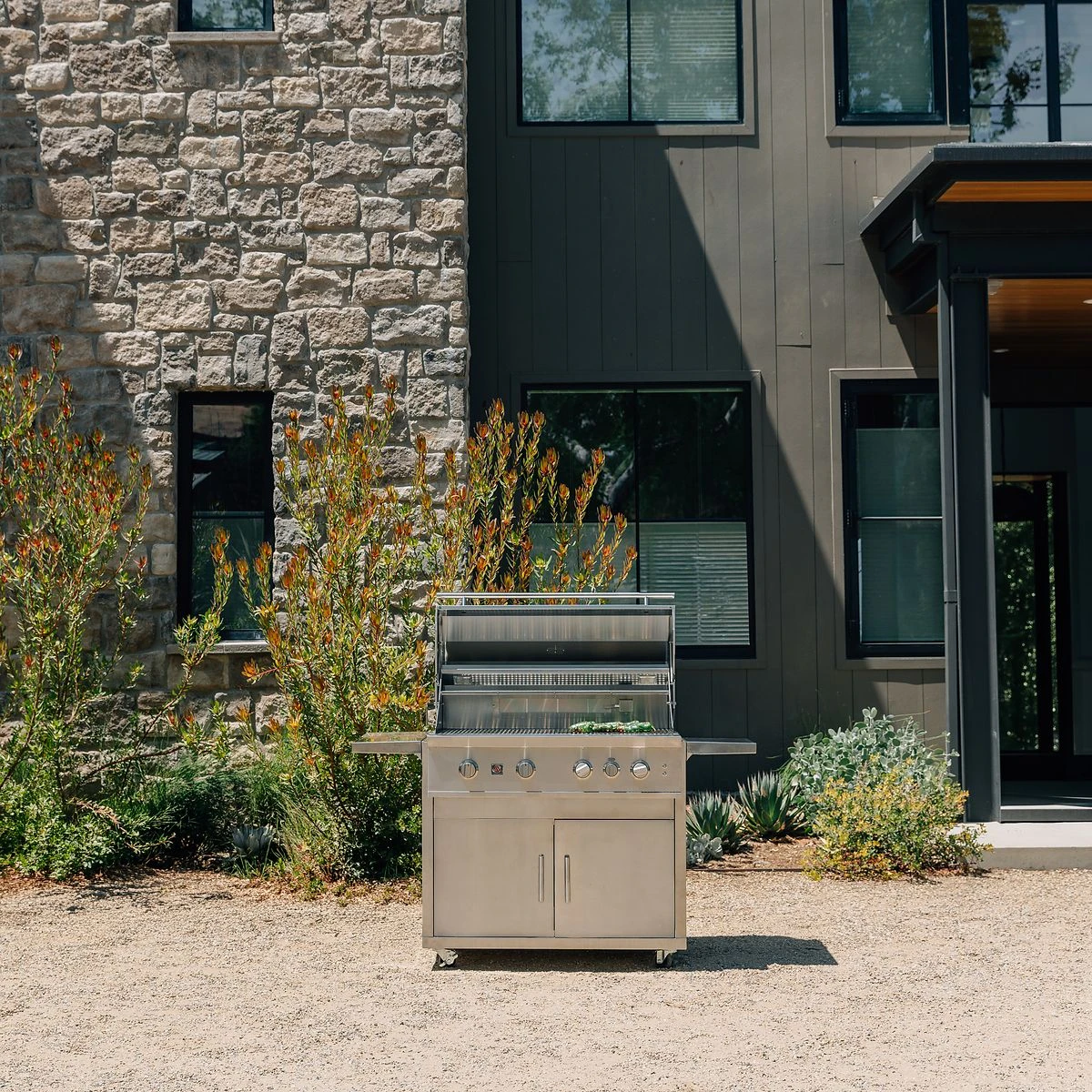 Summerset Sizzler 40-inch freestanding gas grill on a gravel patio outside a modern home with stone and dark vertical siding